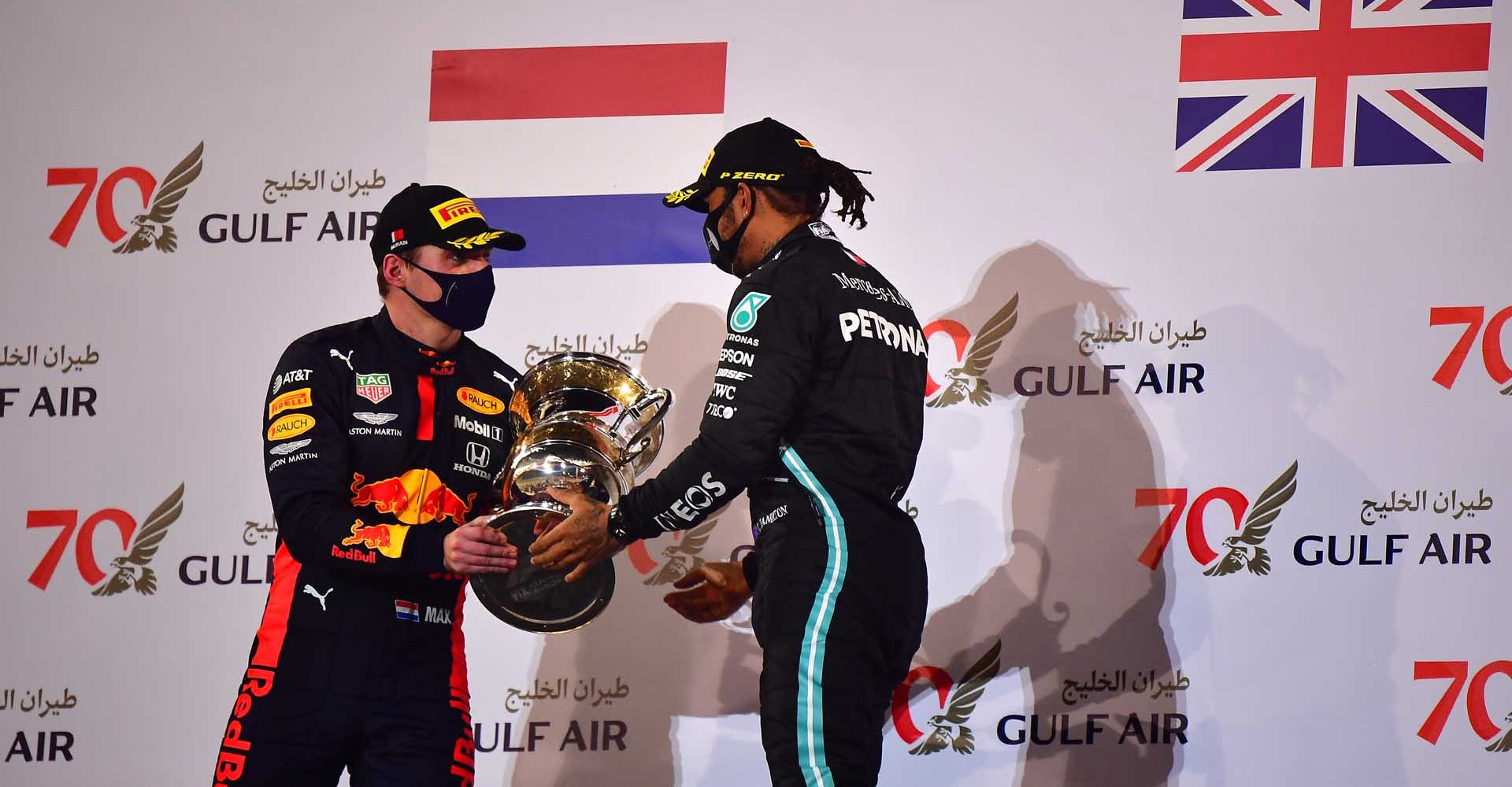 BAHRAIN, BAHRAIN - NOVEMBER 29: Race winner Lewis Hamilton of Great Britain and Mercedes GPreceives a trophy on the podium from Second placed Max Verstappen of Netherlands and Red Bull Racing celebrates on the podium during the F1 Grand Prix of Bahrain at Bahrain International Circuit on November 29, 2020 in Bahrain, Bahrain. (Photo by Giuseppe Cacace - Pool/Getty Images)