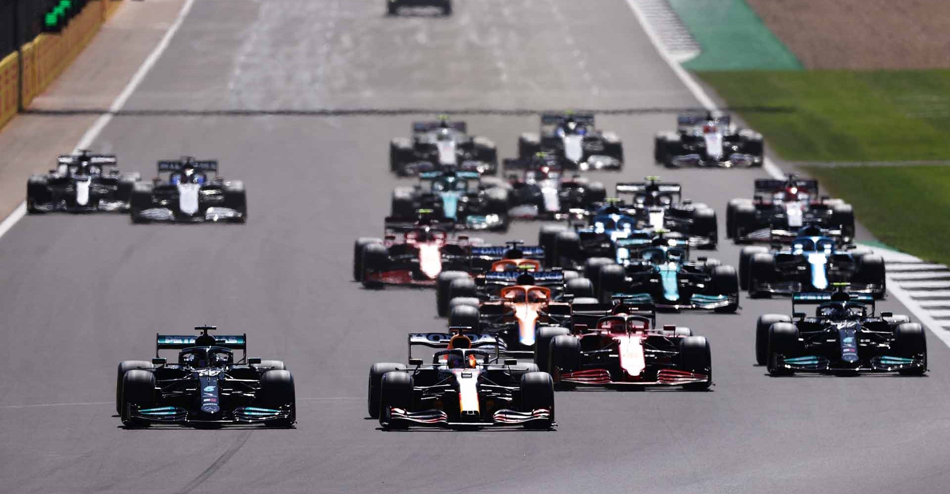 NORTHAMPTON, ENGLAND - JULY 18: Lewis Hamilton of Great Britain driving the (44) Mercedes AMG Petronas F1 Team Mercedes W12 and Max Verstappen of the Netherlands driving the (33) Red Bull Racing RB16B Honda lead the field into turn one at the start during the F1 Grand Prix of Great Britain at Silverstone on July 18, 2021 in Northampton, England. (Photo by Lars Baron/Getty Images)